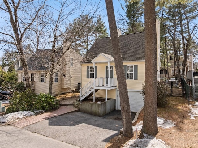 view of front of property featuring a chimney, driveway, an attached garage, a shingled roof, and stairs