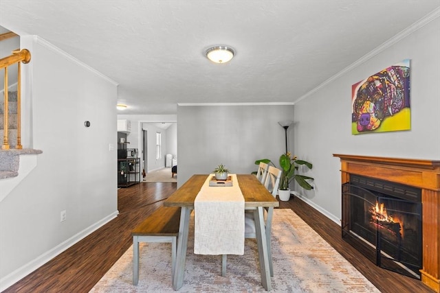 dining area with a warm lit fireplace, wood finished floors, stairs, and ornamental molding