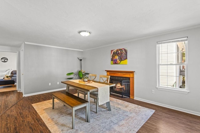 dining area with baseboards, a lit fireplace, wood finished floors, and ornamental molding