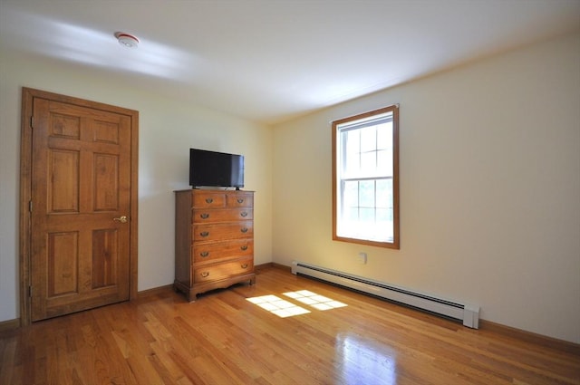 unfurnished bedroom featuring light wood finished floors and a baseboard heating unit