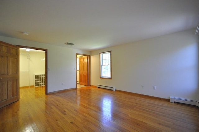 empty room with baseboards, a baseboard heating unit, light wood finished floors, and visible vents