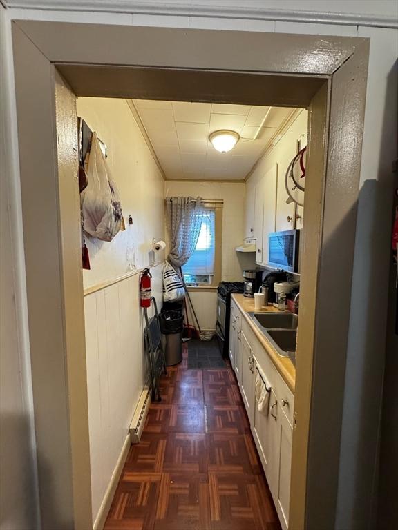 kitchen featuring black gas stove, white cabinetry, a sink, and a baseboard radiator