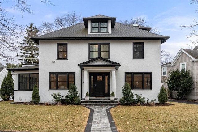 american foursquare style home featuring stucco siding, a shingled roof, and a front lawn