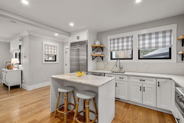 kitchen featuring light wood finished floors, light stone countertops, stainless steel built in fridge, white cabinets, and a sink