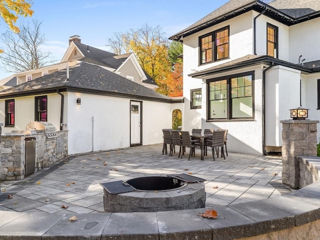 back of house featuring a patio, an outdoor kitchen, outdoor dining area, stucco siding, and a fire pit