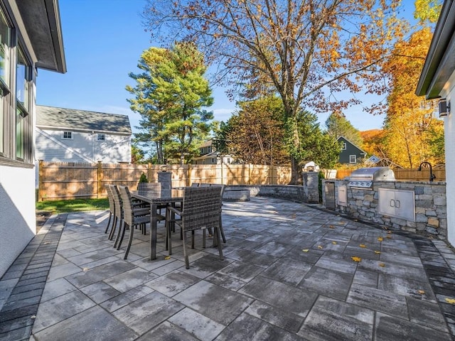 view of patio featuring an outdoor kitchen, area for grilling, outdoor dining area, a fenced backyard, and a sink