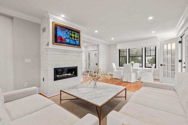 living area with a tiled fireplace, recessed lighting, crown molding, and light wood-type flooring