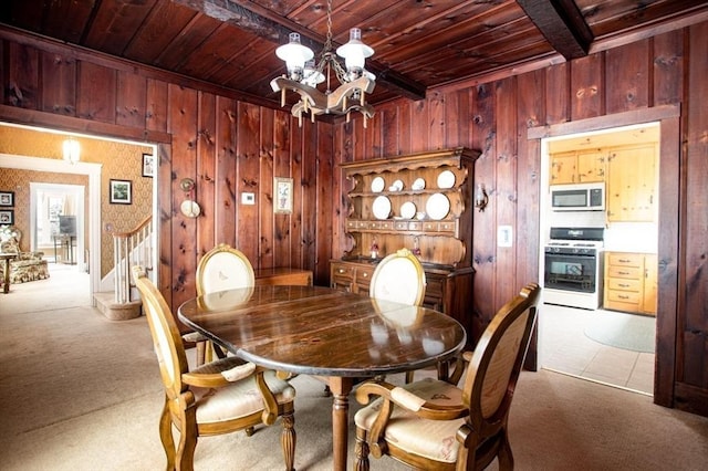 carpeted dining area with a notable chandelier, wooden ceiling, and wood walls