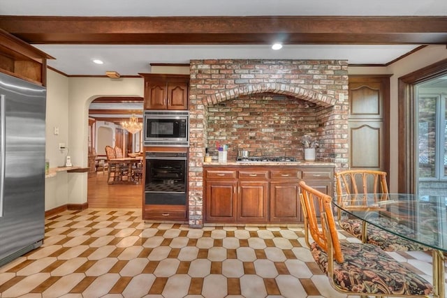 kitchen with ornamental molding, beamed ceiling, a chandelier, and appliances with stainless steel finishes