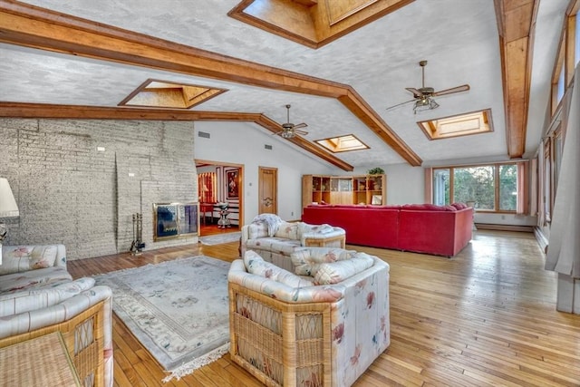 living room with light wood-type flooring, brick wall, vaulted ceiling with skylight, ceiling fan, and a fireplace