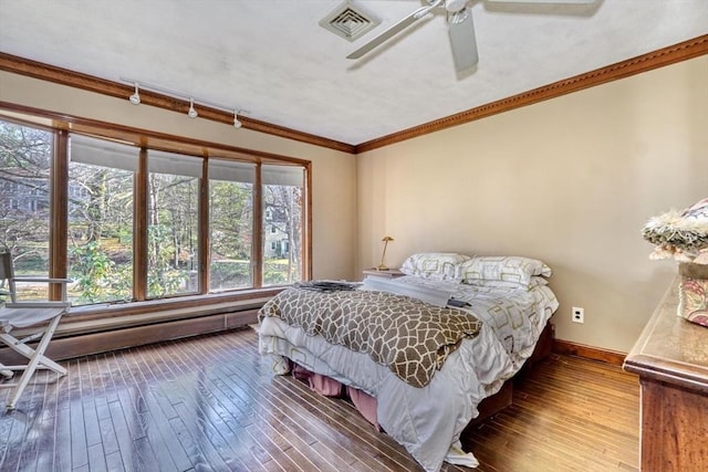 bedroom with a baseboard heating unit, rail lighting, crown molding, ceiling fan, and wood-type flooring