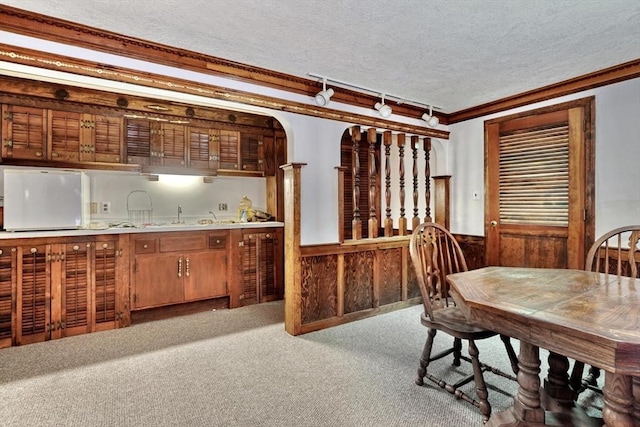 carpeted dining area featuring ornamental molding, a textured ceiling, wooden walls, and sink