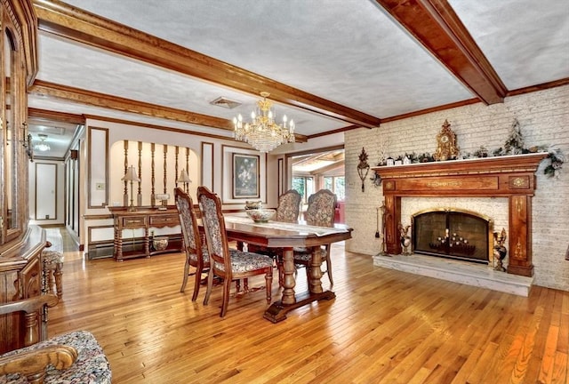 dining area featuring beamed ceiling, an inviting chandelier, brick wall, and light hardwood / wood-style flooring