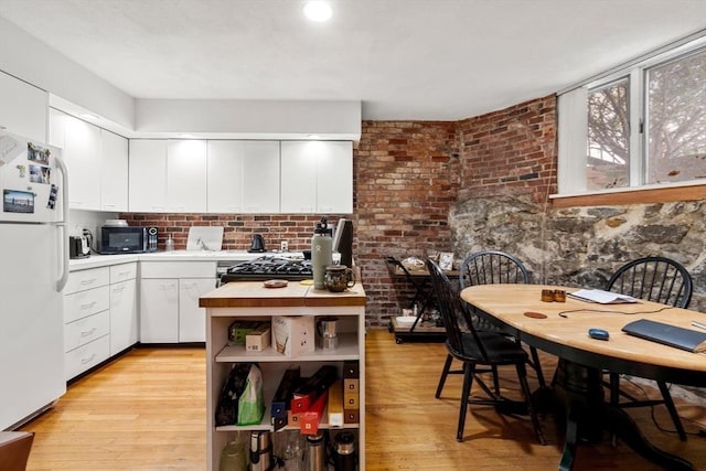 kitchen with black microwave, light wood-style flooring, white cabinetry, light countertops, and freestanding refrigerator