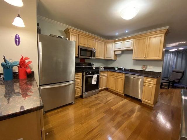 kitchen with ornamental molding, dark countertops, a sink, dark wood finished floors, and appliances with stainless steel finishes