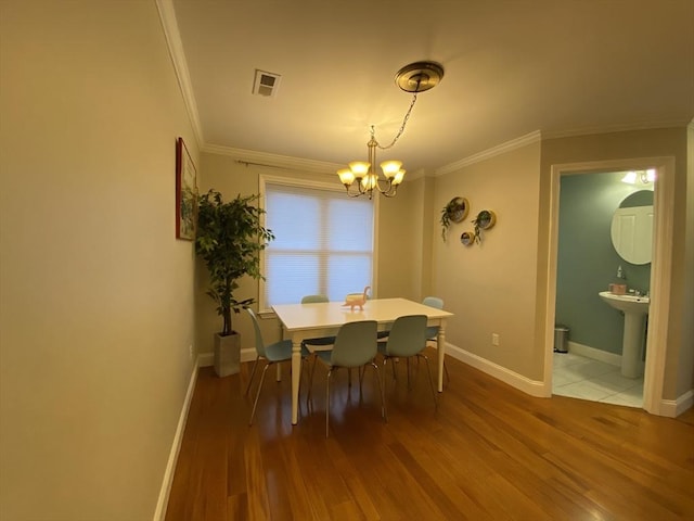 dining room featuring an inviting chandelier, crown molding, wood finished floors, and visible vents