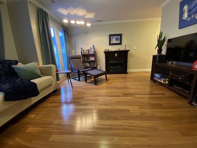 living area featuring baseboards, ornamental molding, wood finished floors, and a fireplace