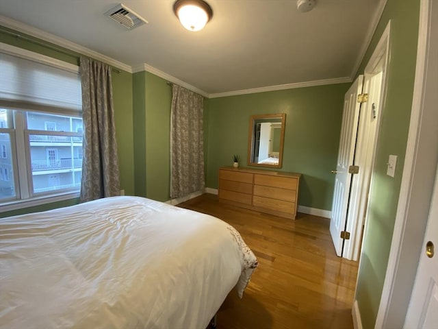 bedroom with baseboards, ornamental molding, wood finished floors, and visible vents