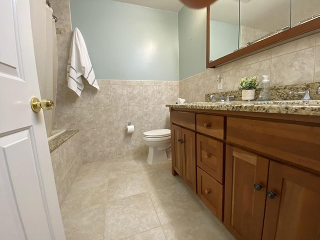 bathroom with tile patterned flooring, vanity, wainscoting, toilet, and tile walls