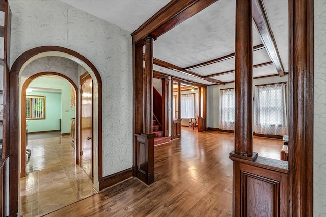 corridor featuring wallpapered walls, baseboards, arched walkways, light wood-style floors, and stairs