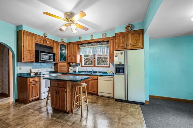 kitchen featuring a kitchen bar, dark countertops, brown cabinetry, arched walkways, and white appliances