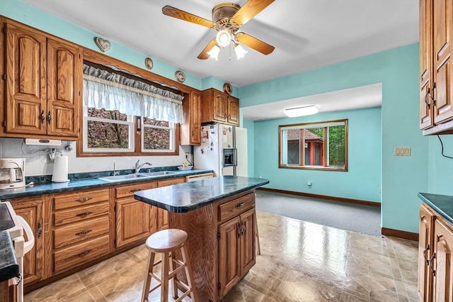kitchen featuring a sink, brown cabinets, a ceiling fan, white refrigerator with ice dispenser, and dark countertops