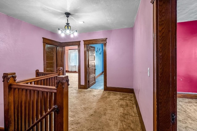 hall with carpet floors, baseboards, and a notable chandelier