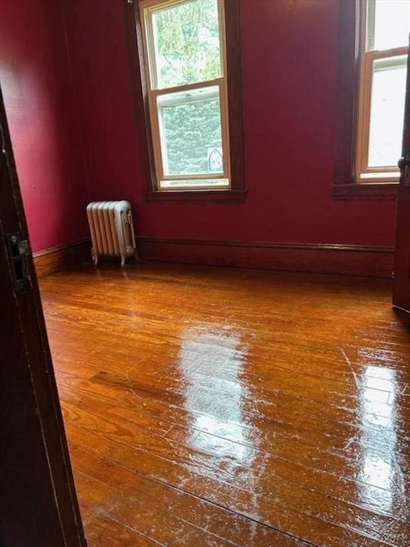 empty room with a wealth of natural light, baseboards, hardwood / wood-style floors, and radiator heating unit
