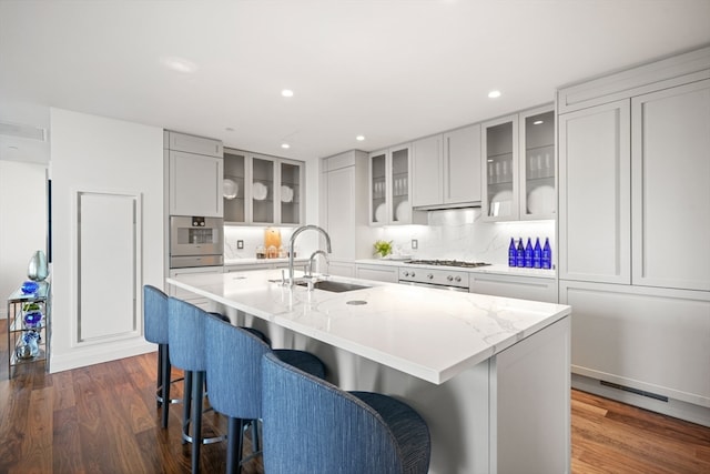 kitchen with dark wood-type flooring, a kitchen bar, sink, a center island with sink, and oven