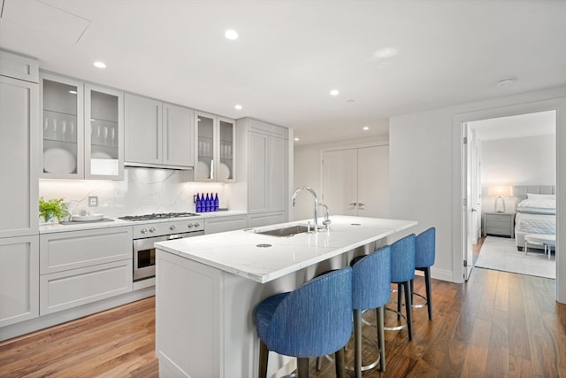 kitchen featuring an island with sink, sink, white cabinets, oven, and hardwood / wood-style flooring