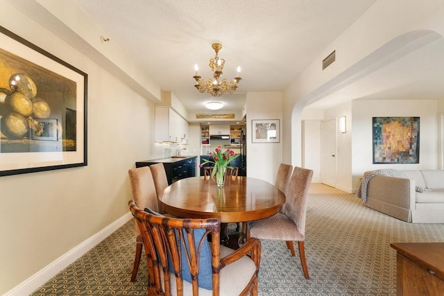carpeted dining room featuring arched walkways, a chandelier, baseboards, and a sink