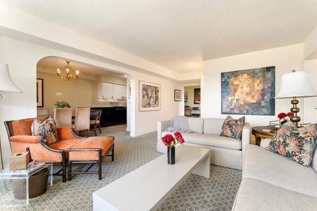carpeted living room featuring arched walkways and a chandelier