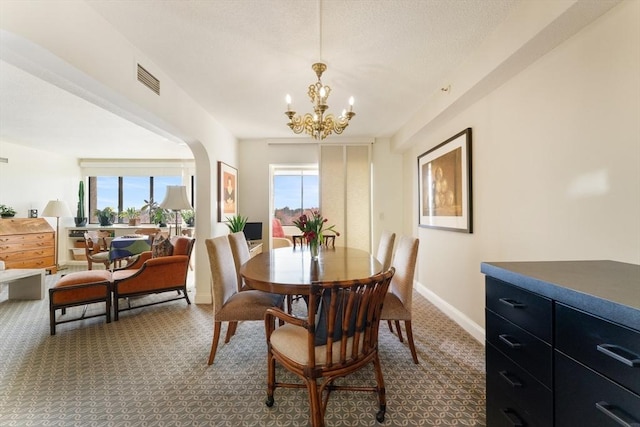 carpeted dining area with healthy amount of natural light, a chandelier, baseboards, and arched walkways