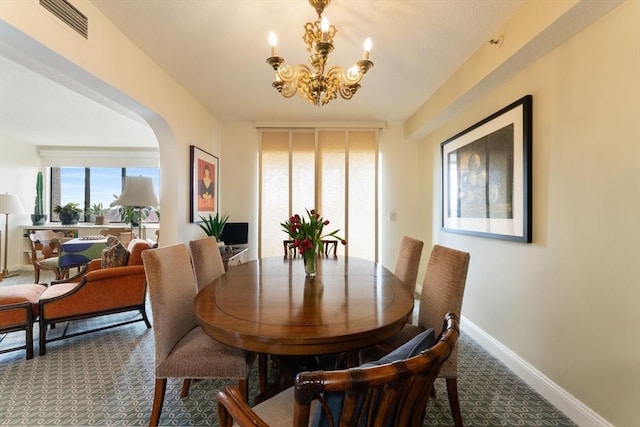 dining room featuring a chandelier, arched walkways, carpet floors, and baseboards