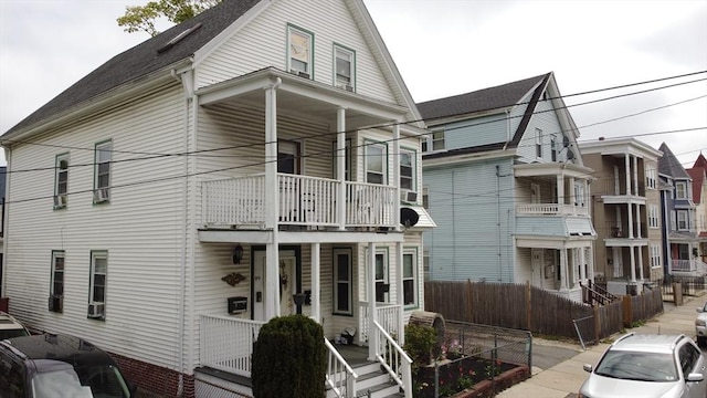 view of front facade featuring a balcony, a porch, and fence