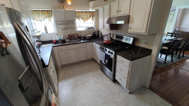 kitchen featuring a sink, under cabinet range hood, white cabinetry, dark countertops, and appliances with stainless steel finishes