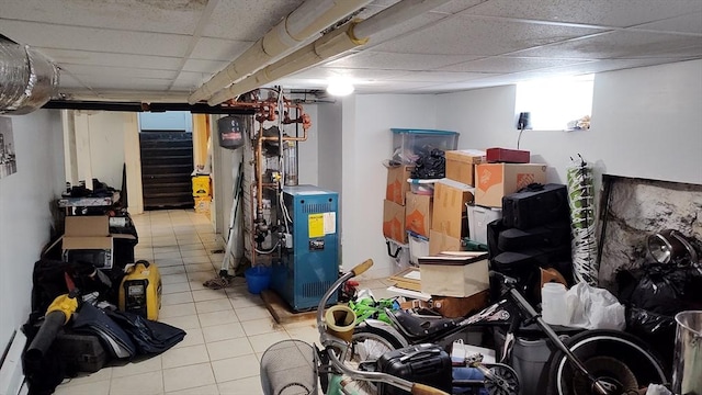 finished basement with stairs, a drop ceiling, tile patterned flooring, and a heating unit