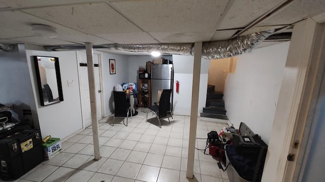 finished basement featuring freestanding refrigerator, stairs, and light tile patterned floors