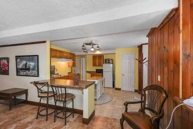 kitchen with kitchen peninsula, white fridge, light tile flooring, a textured ceiling, and sink