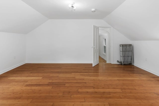 additional living space with hardwood / wood-style floors, lofted ceiling, and radiator heating unit