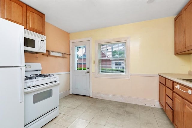 kitchen featuring white appliances, light countertops, baseboards, and brown cabinetry