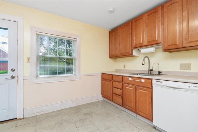 kitchen featuring white dishwasher, a sink, light countertops, baseboards, and brown cabinetry