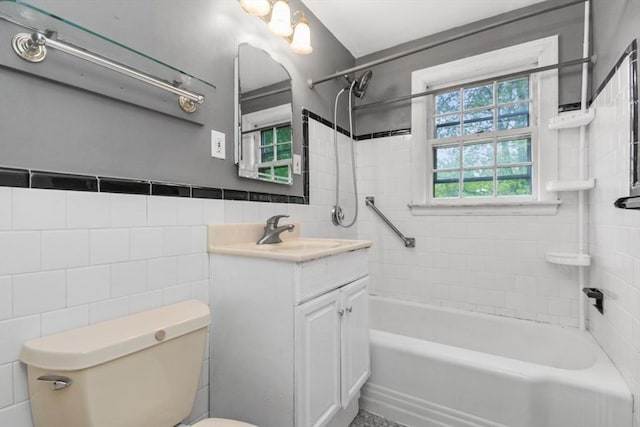 full bath featuring tile walls, toilet, washtub / shower combination, vanity, and wainscoting