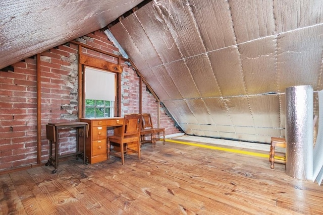 unfurnished office with wood-type flooring, vaulted ceiling, and brick wall