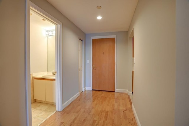 corridor with recessed lighting, a sink, light wood-style flooring, and baseboards