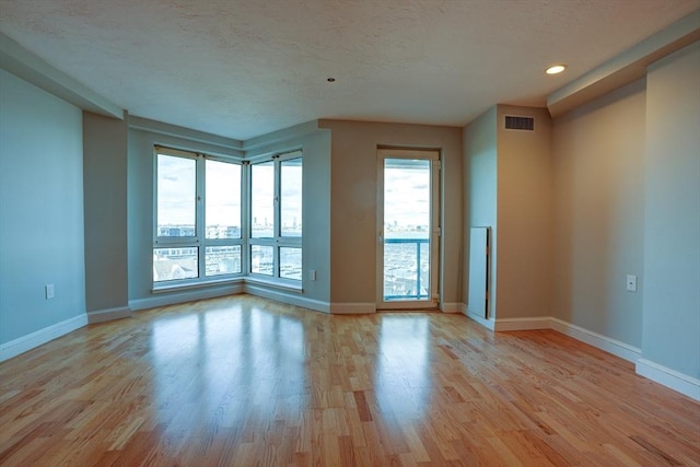 spare room with light wood-type flooring, baseboards, visible vents, and a textured ceiling