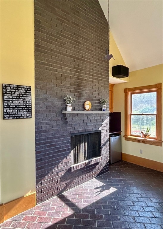 unfurnished living room featuring high vaulted ceiling and a brick fireplace