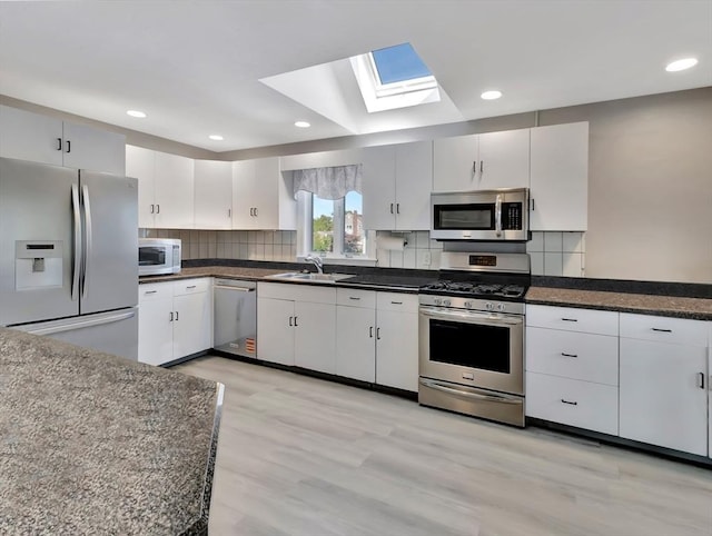 10 Vernon Ave, Hull, MA 02045 - kitchen with stainless steel appliances, a skylight, dark countertops, tasteful backsplash, and light wood-style flooring
