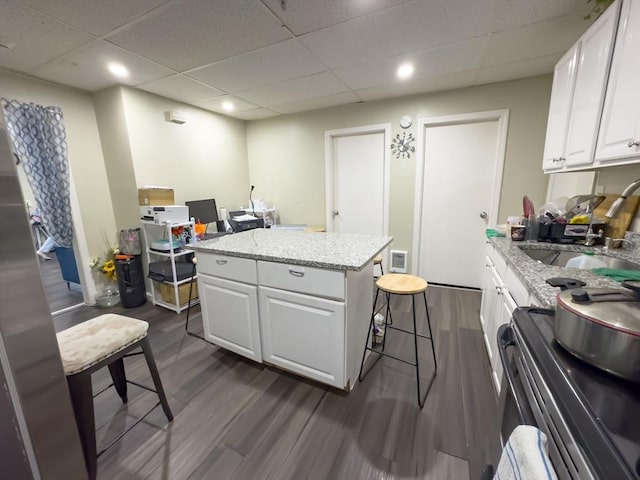 kitchen with a drop ceiling, stainless steel electric stove, white cabinets, dark hardwood / wood-style floors, and a kitchen island