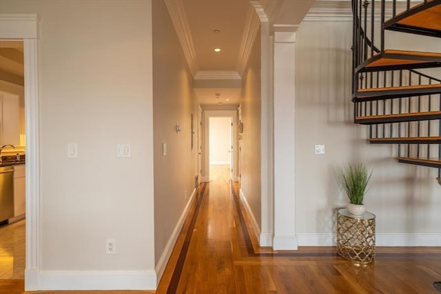 hallway with crown molding, a sink, wood finished floors, and baseboards